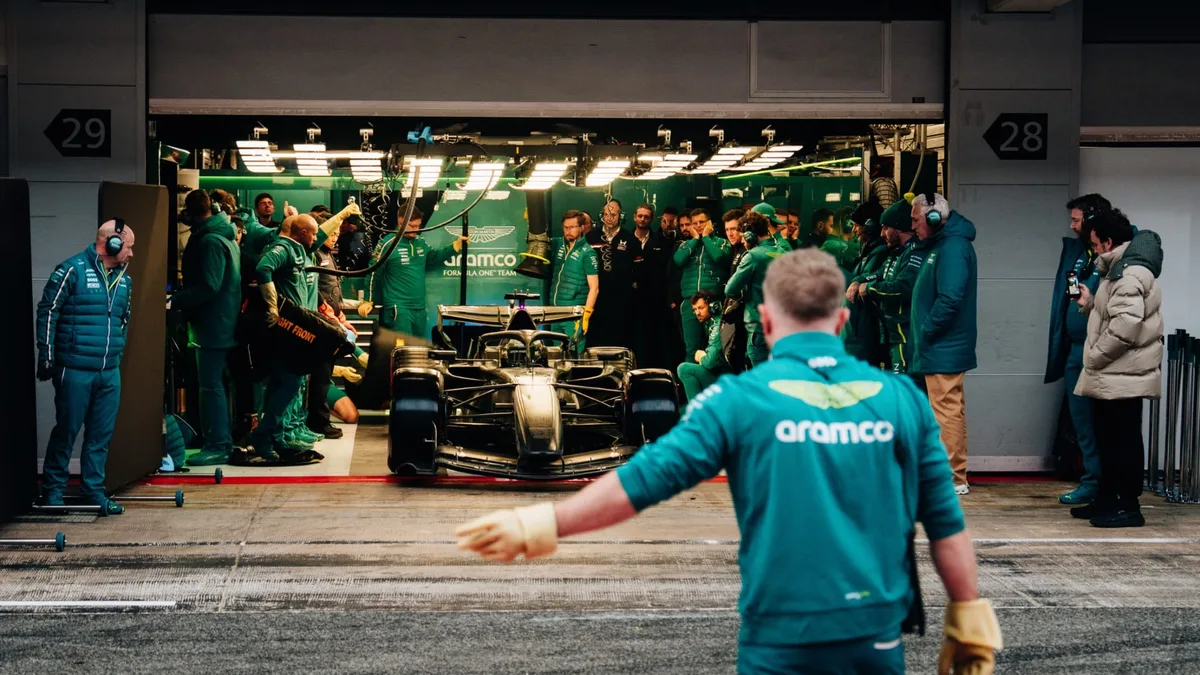 The Aston Martin AMR26 leaves the pit box surrounded by mechanics