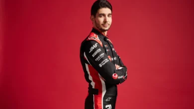 Esteban Ocon in Haas race overalls with his arms folded against a red studio background