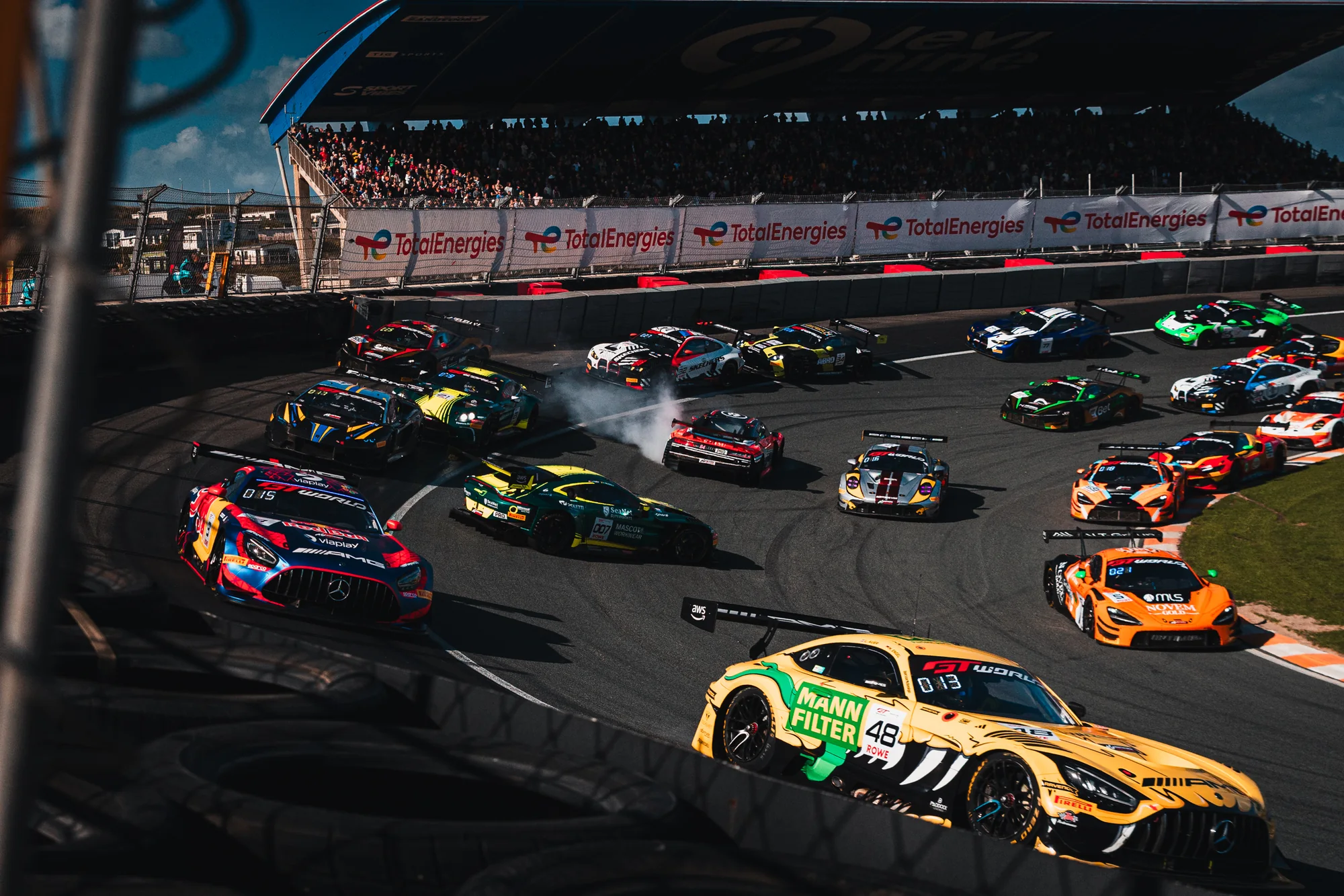 The GT World Challenge Europe field through the banked Hugenholtzbocht at Zandvoort, with the Eastalent Audi of Christopher Haase facing the wrong way in a cloud of tyre smoke