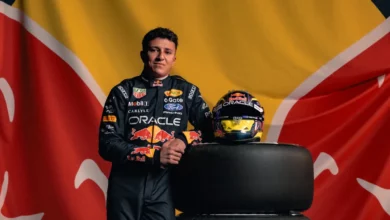 Isack Hadjar in Red Bull race overalls leaning on a stack of Pirelli tyres beside his helmet
