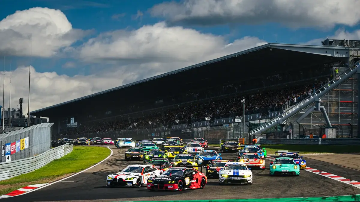 The NLS8 field streams away from the start past a packed grandstand at the Nurburgring
