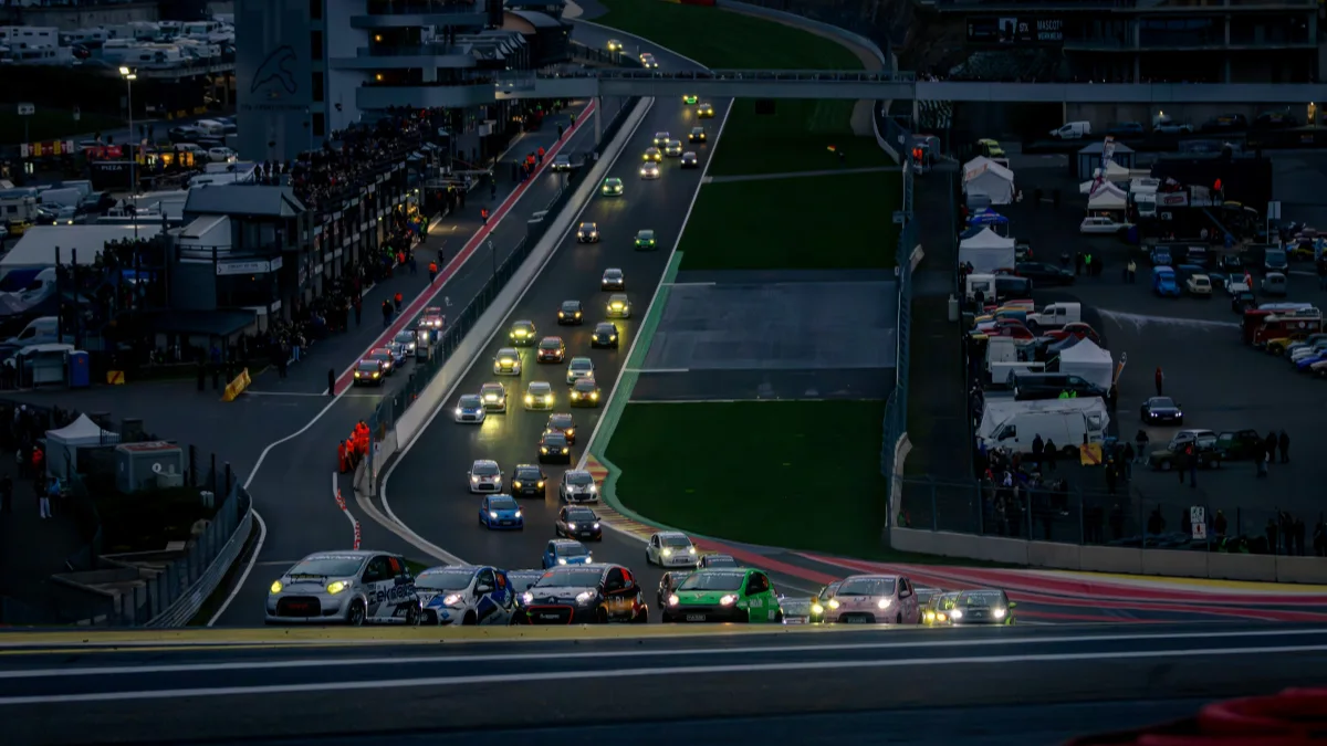 Citroen C1s and 2CVs with headlights on, racing in a long line at Spa-Francorchamps