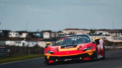 A red and yellow Ferrari 296 GT3 with number 51 on track at Zandvoort, with dune houses behind