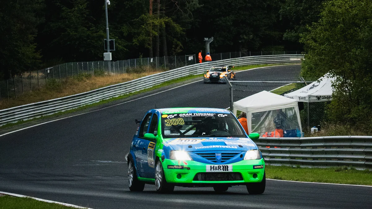 The green and blue number 300 Ollis Garage Racing Dacia Logan on the Nordschleife with Nürburg castle in the distance