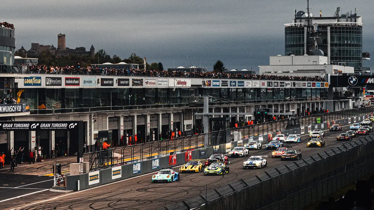 The NLS9 field heading down the start-finish straight past the pit building with Nürburg castle on the hill behind