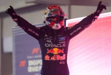 Max Verstappen in his helmet raises both arms in parc ferme after winning in Singapore