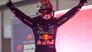 Max Verstappen in his helmet raises both arms in parc ferme after winning in Singapore