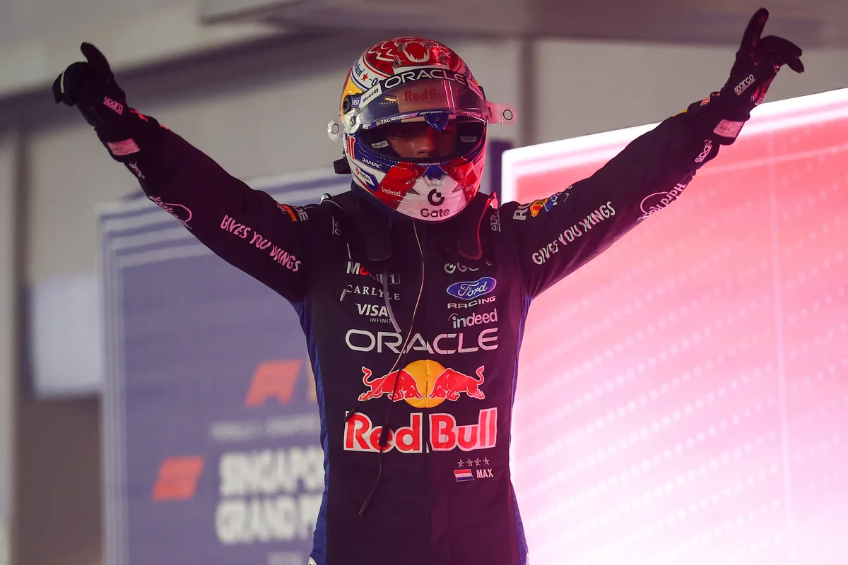 Max Verstappen in his helmet raises both arms in parc ferme after winning in Singapore